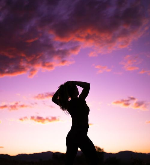 Person meditating during a vibrant sunrise over mountains.